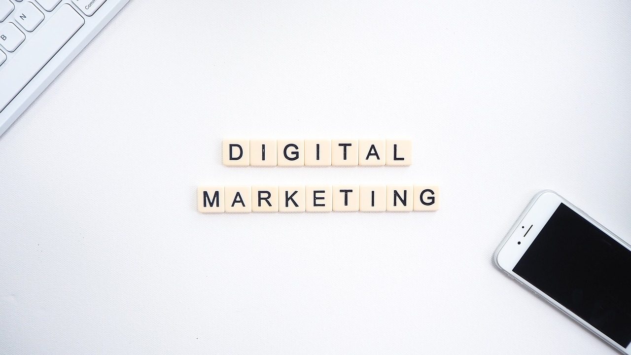 crabble tiles spelling out 'Digital Marketing' on a white desk with a smartphone and keyboard nearby